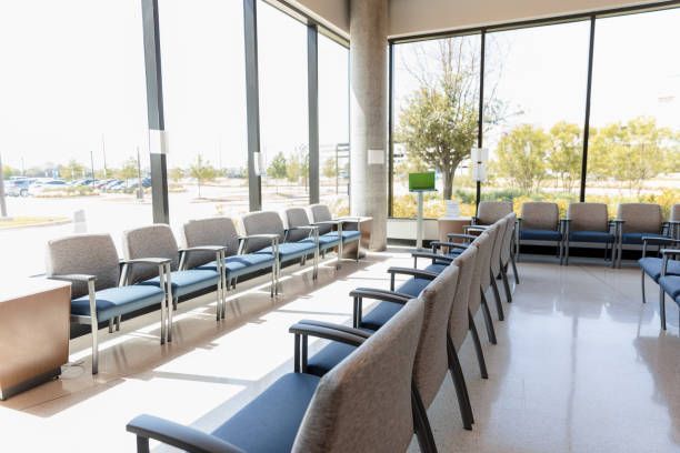 Waiting room with rows of empty chairs facing a large window overlooking a parking lot and trees