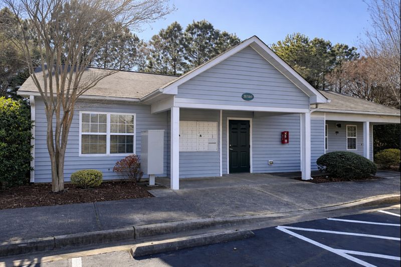 A light blue single-story office building with a front porch, a dark entrance door, and a communal mailbox cluster.