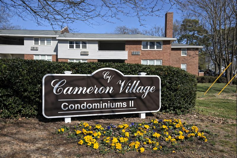 A sign for Cameron Village Condominiums II in front of a brick apartment building with yellow flowers in the foreground.