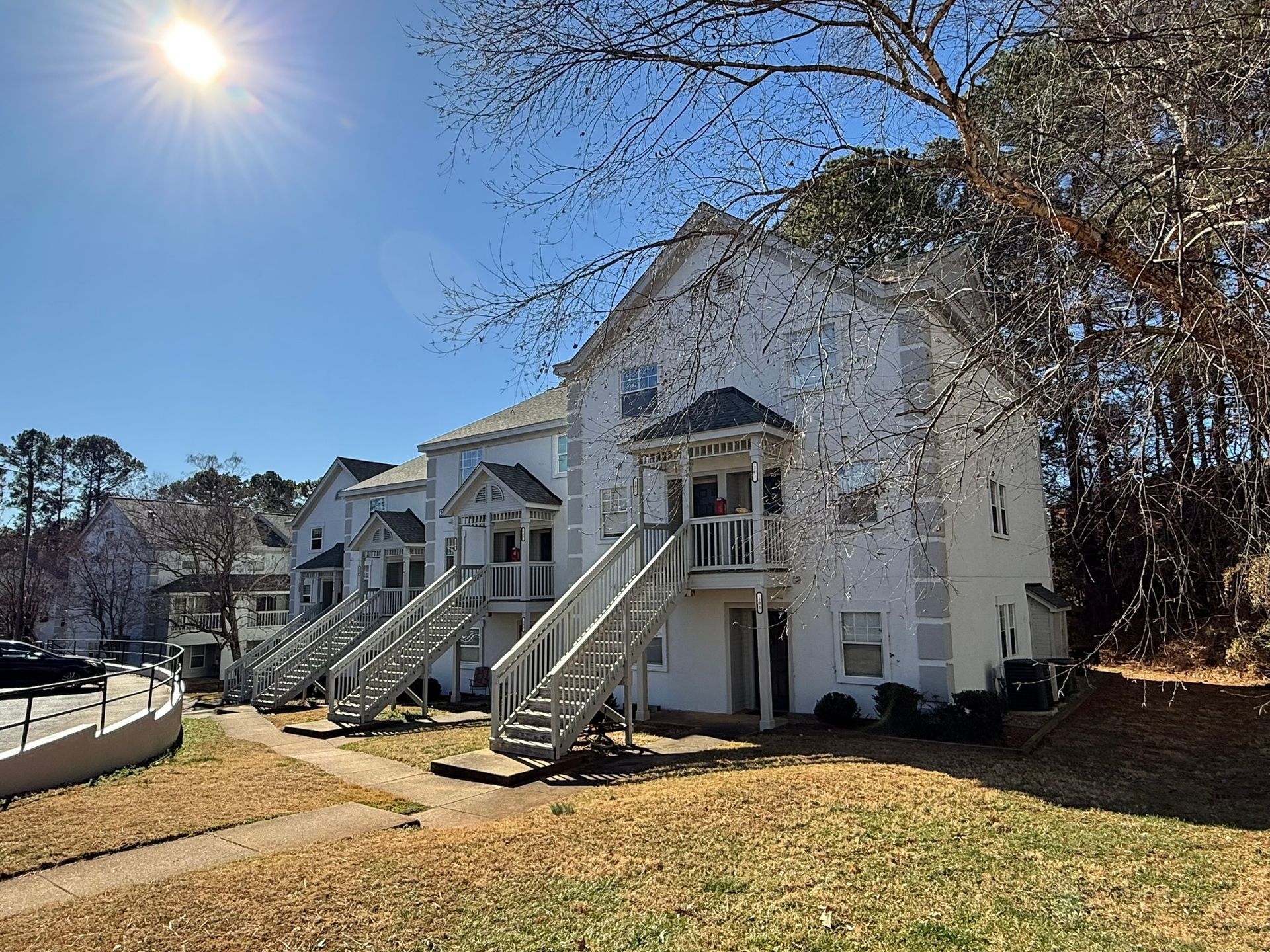 Two white, multi-story apartment buildings with outdoor staircases set against a sunny, clear blue sky.