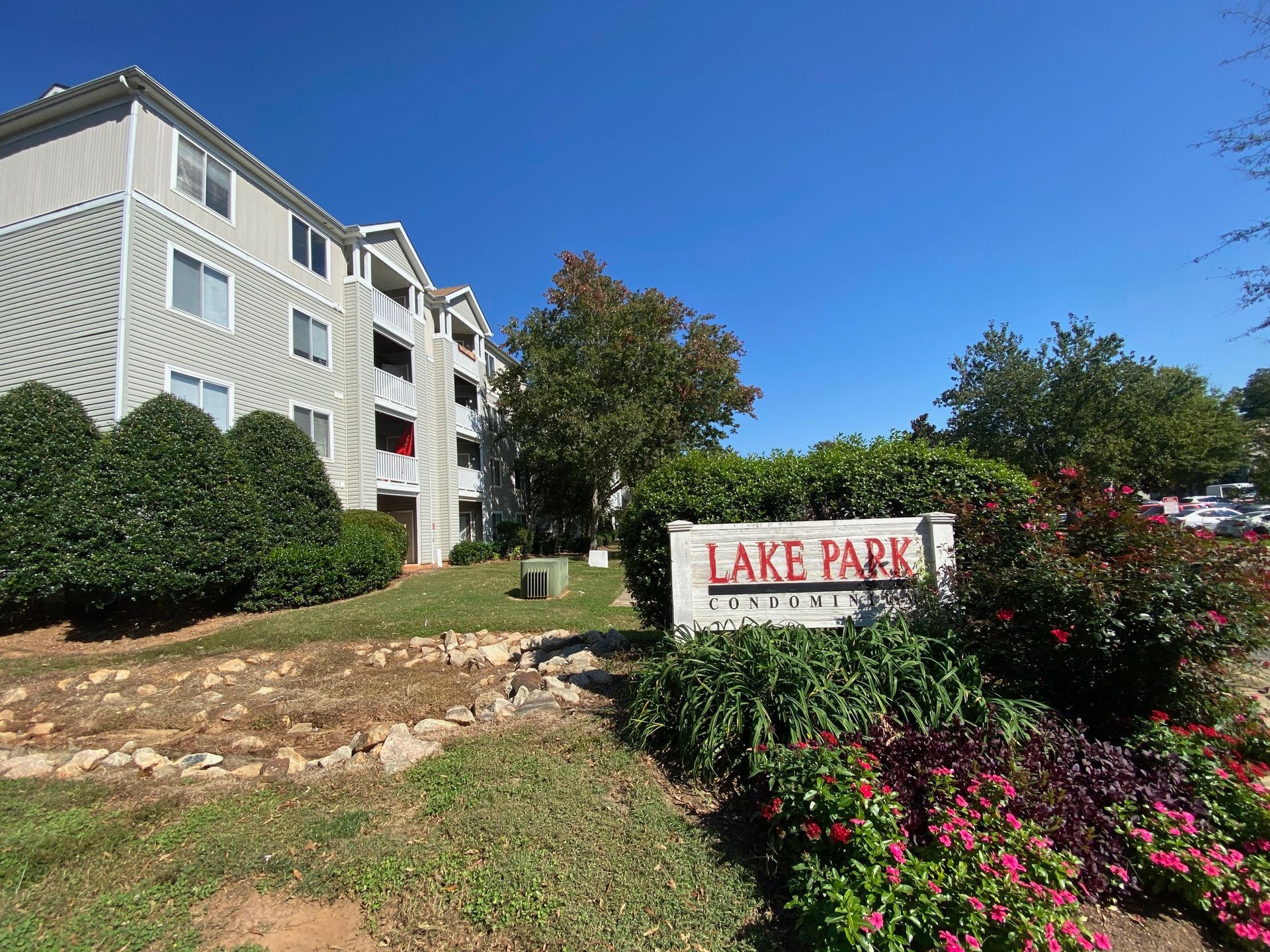 A stone sign labeled Lake Park Apartments in front of a three-story light-colored apartment building under a blue sky.