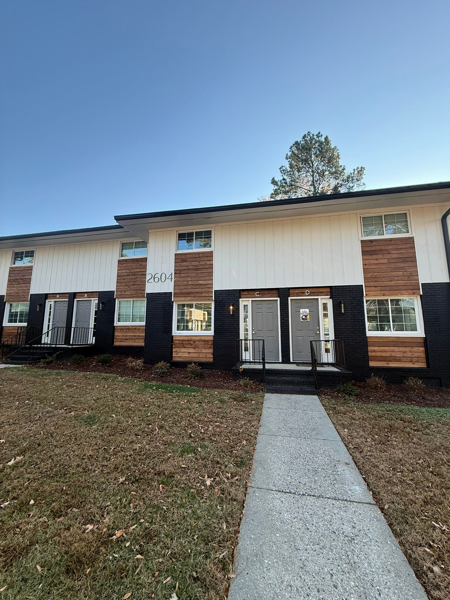 A two-story apartment building with a white upper level, wood-paneled accents, and a dark base, with a front walkway.