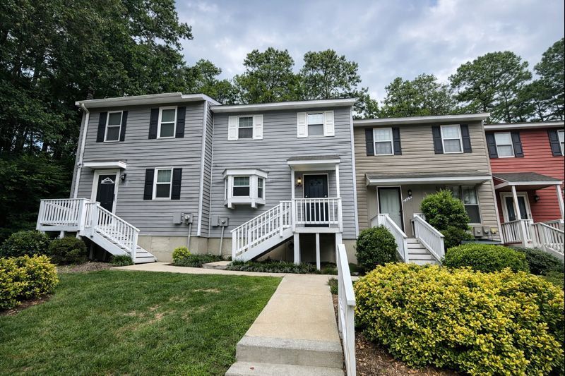 A row of multi-story townhomes with grey and tan vinyl siding, white railings, and front-facing staircases.
