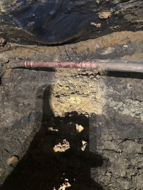 A shadow of a person is cast on the ground next to a pipe