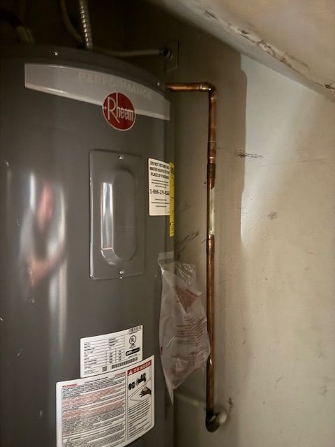 A gray water heater is sitting on a wall next to a copper pipe