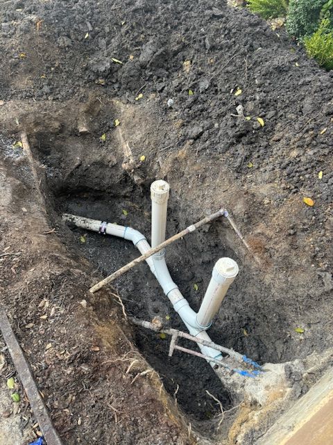 A bunch of pipes are laying in the dirt in a hole