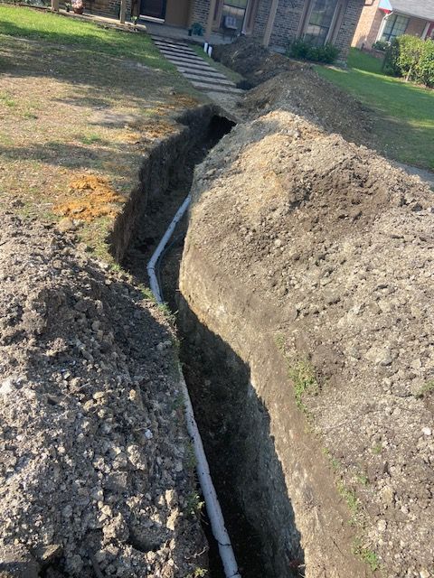 A pipe is being installed in a trench in front of a house