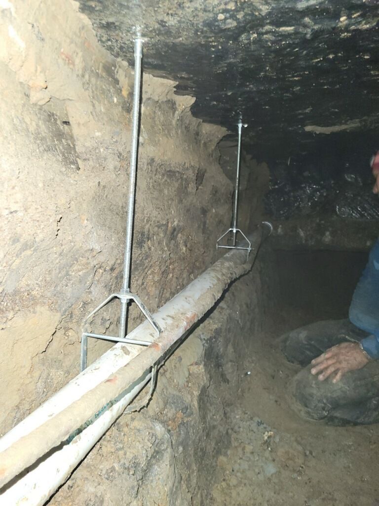 A man is kneeling down in a cave with a pipe hanging from the ceiling