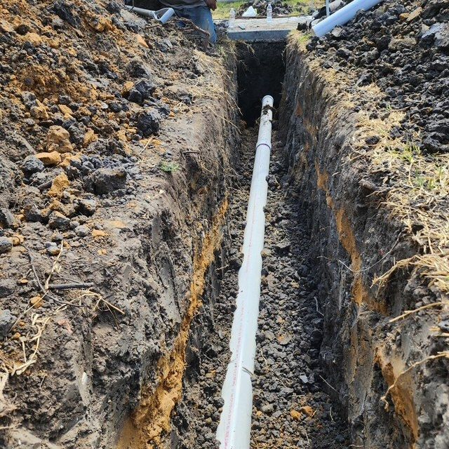 A white pipe is being installed in a trench
