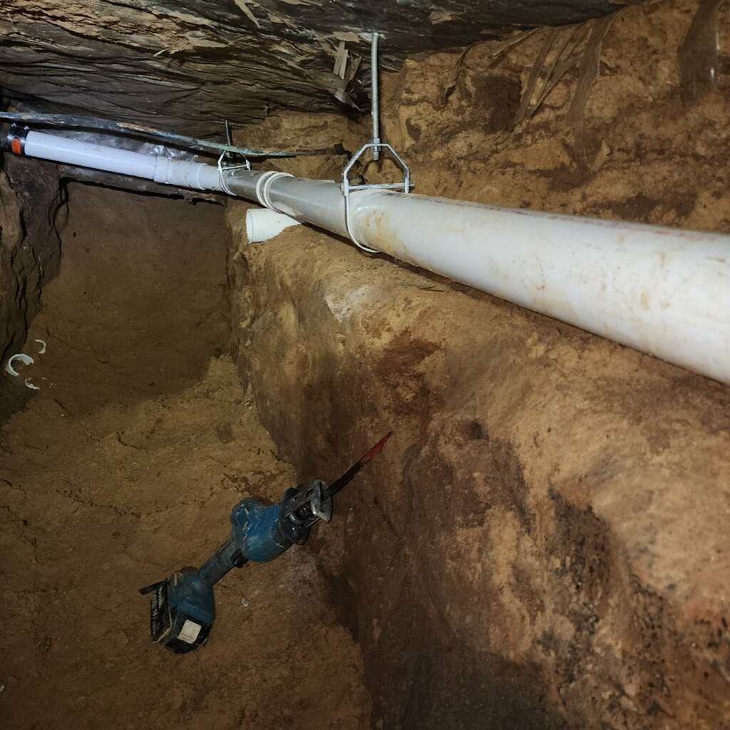 A drill is sitting in the dirt next to a pipe