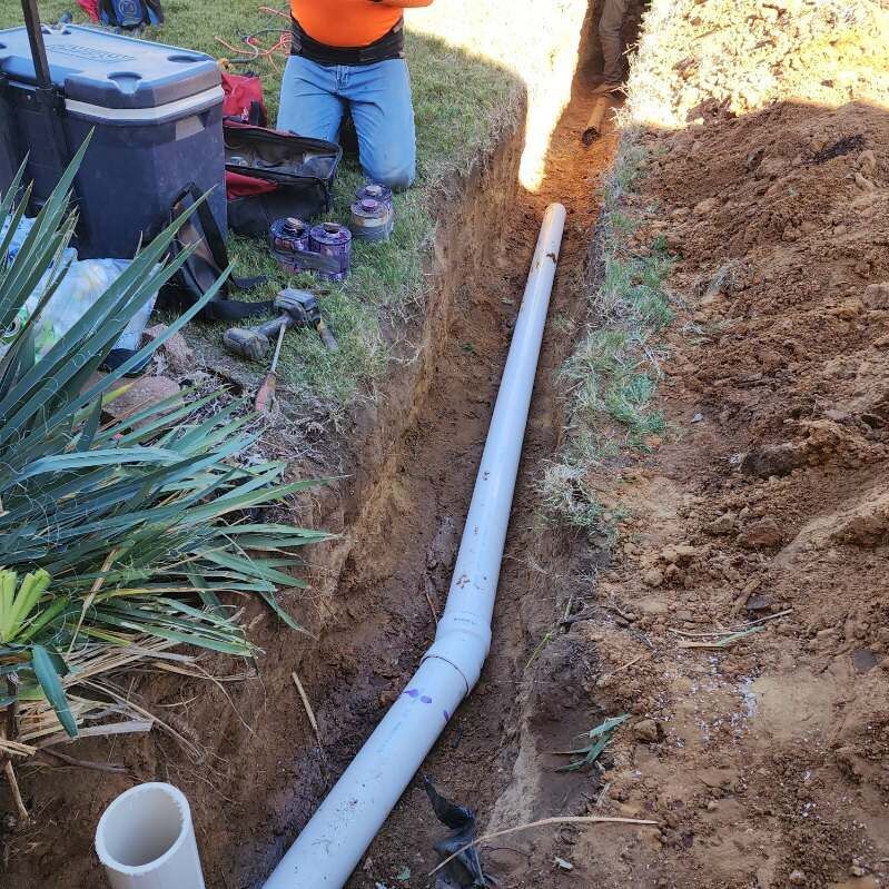 A man is kneeling in the dirt next to a pipe