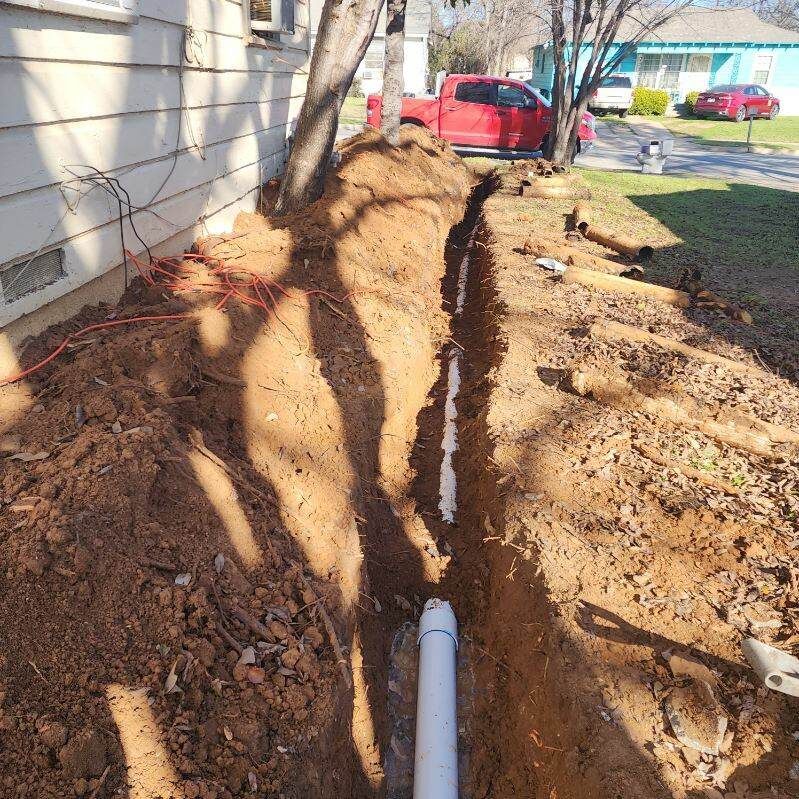 A white pipe is being installed in the dirt next to a house