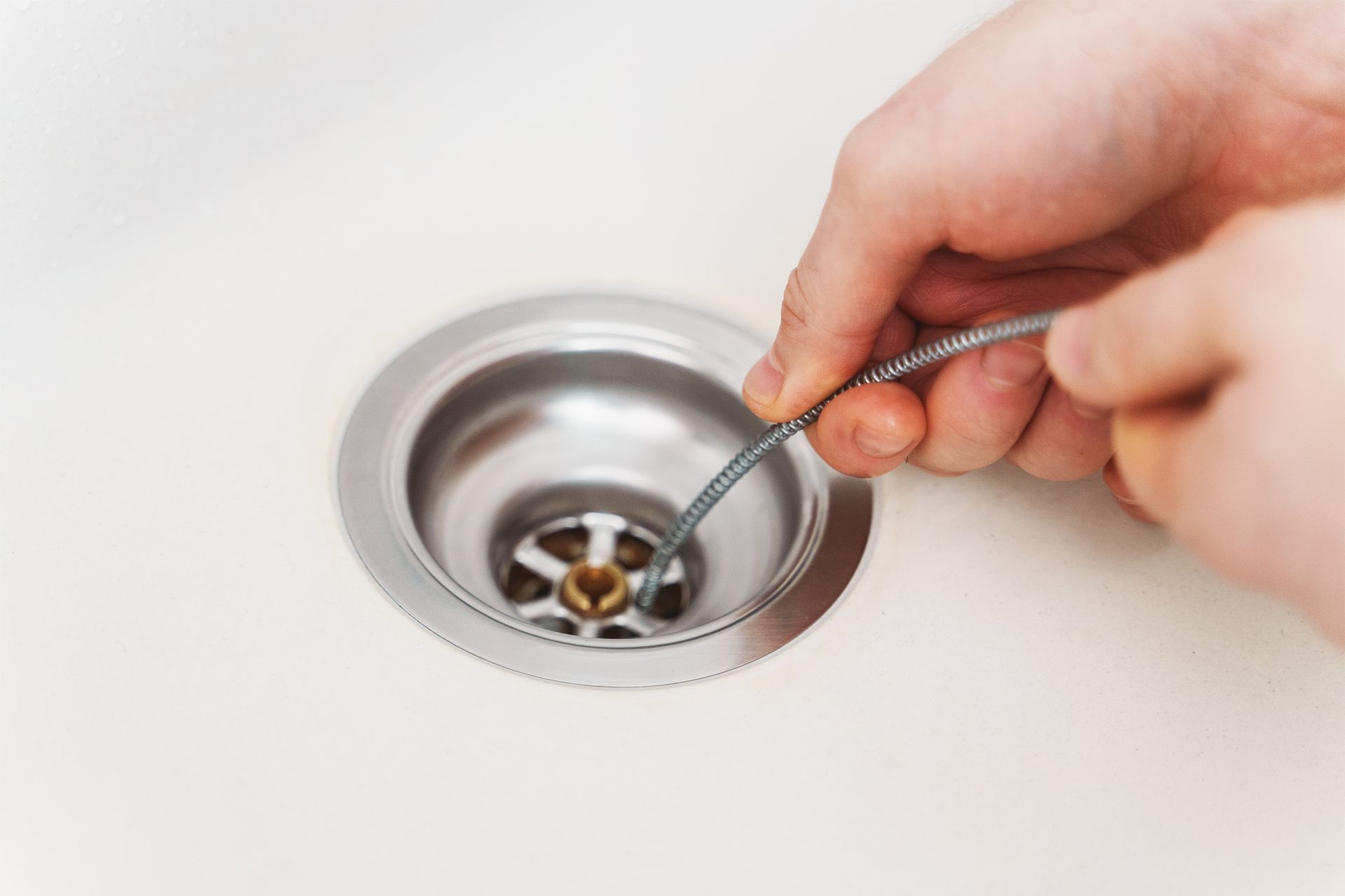 A person is cleaning a sink drain with a wire.
