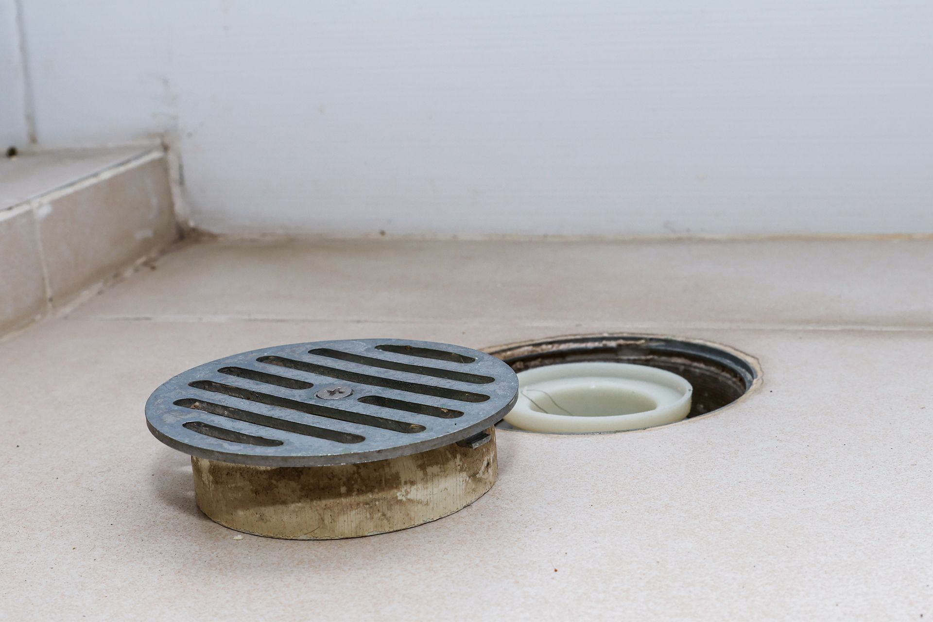 A drain cover is sitting on a tiled floor next to a hole in the floor.
