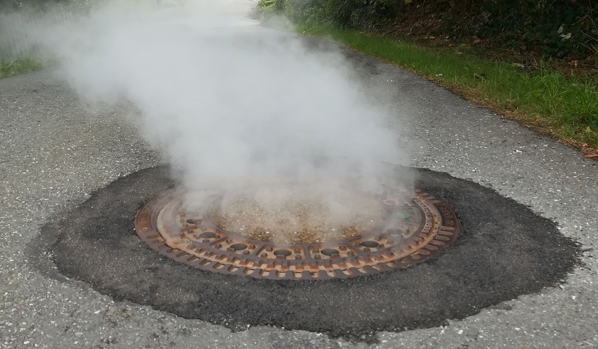 Smoke is coming out of a manhole cover on a road