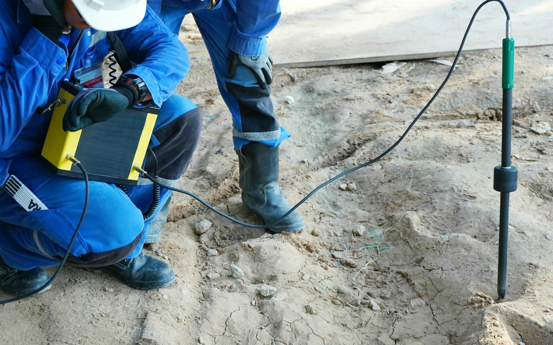 A man is kneeling down in the sand using a device