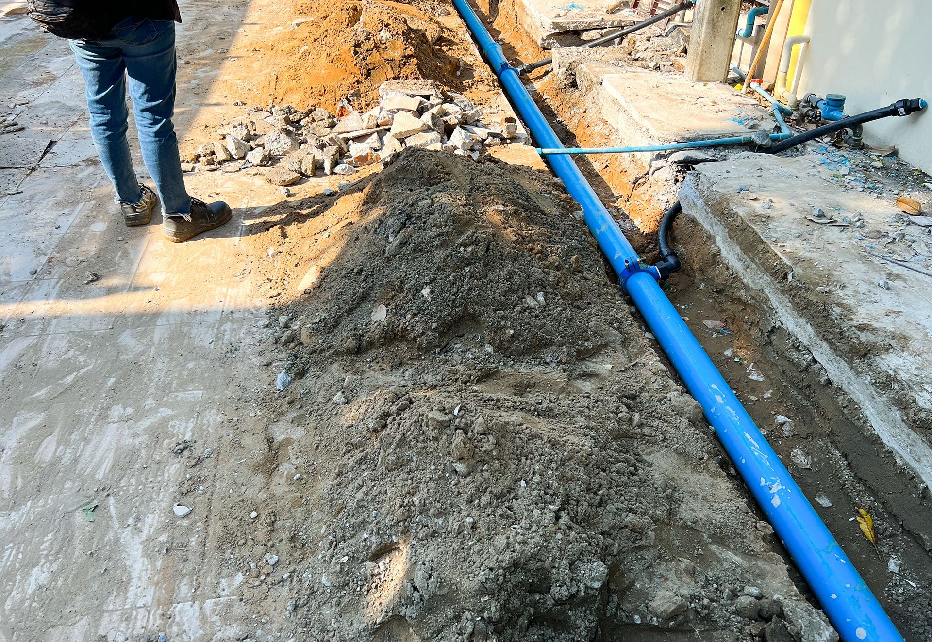 A man is standing next to a blue pipe in the dirt