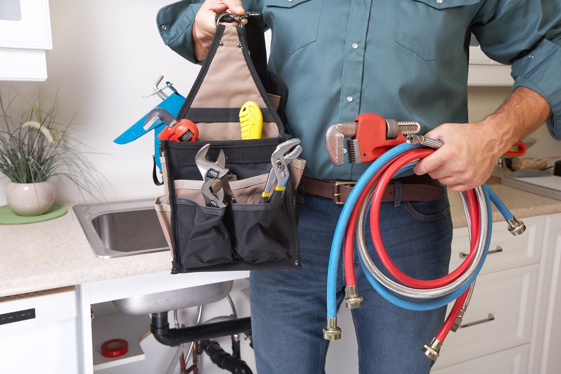A plumber is holding a hose and a tool bag