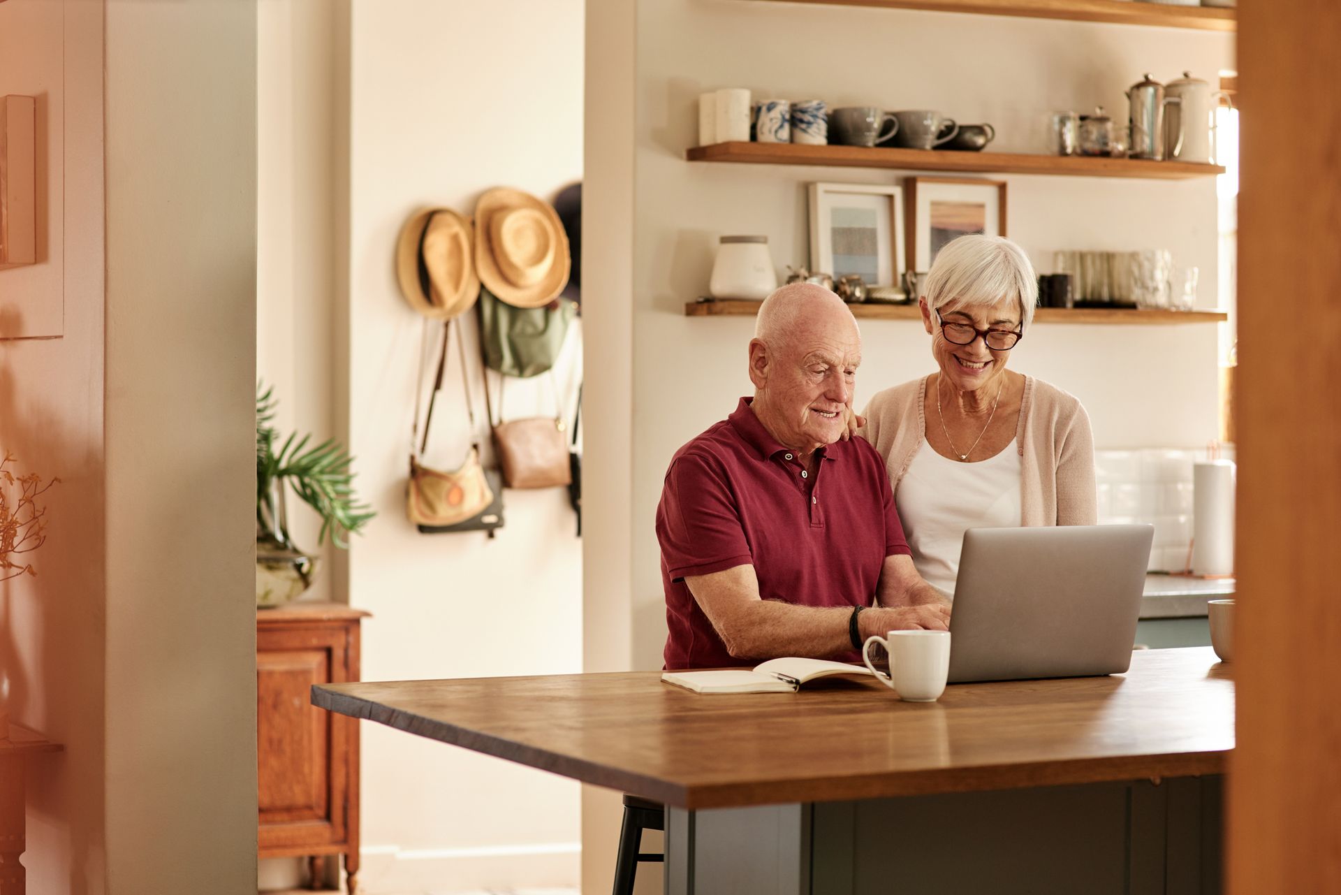Senior couple looking at a laptop in a kitchen setting. Man points, woman smiles.