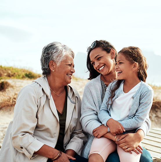 Three women smiling, sitting close together outdoors.