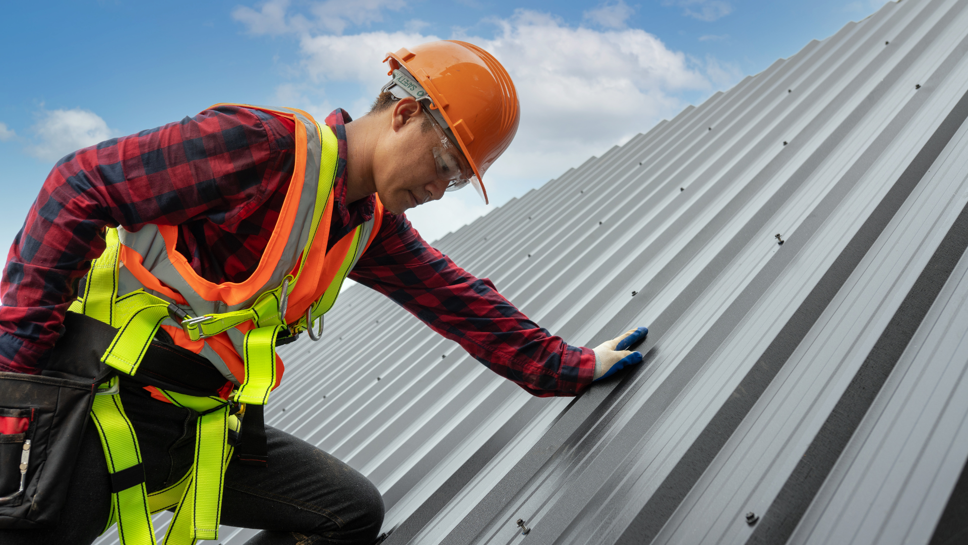A man wearing a hard hat and safety harness is working on a roof.