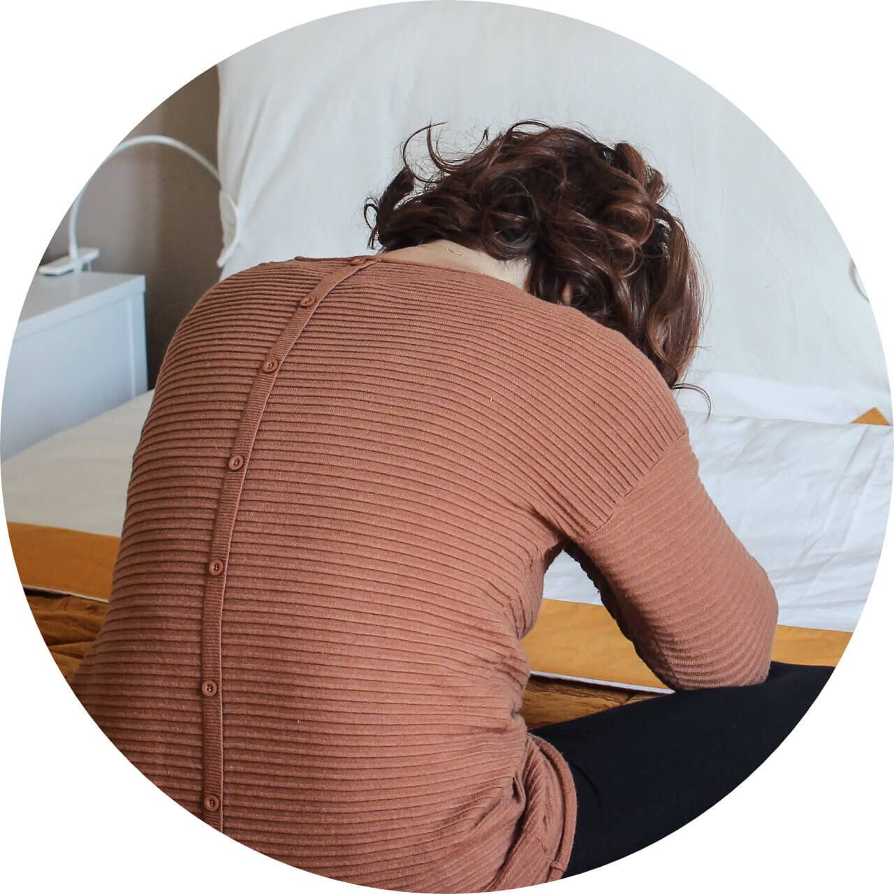 A woman is sitting on a bed with her head down