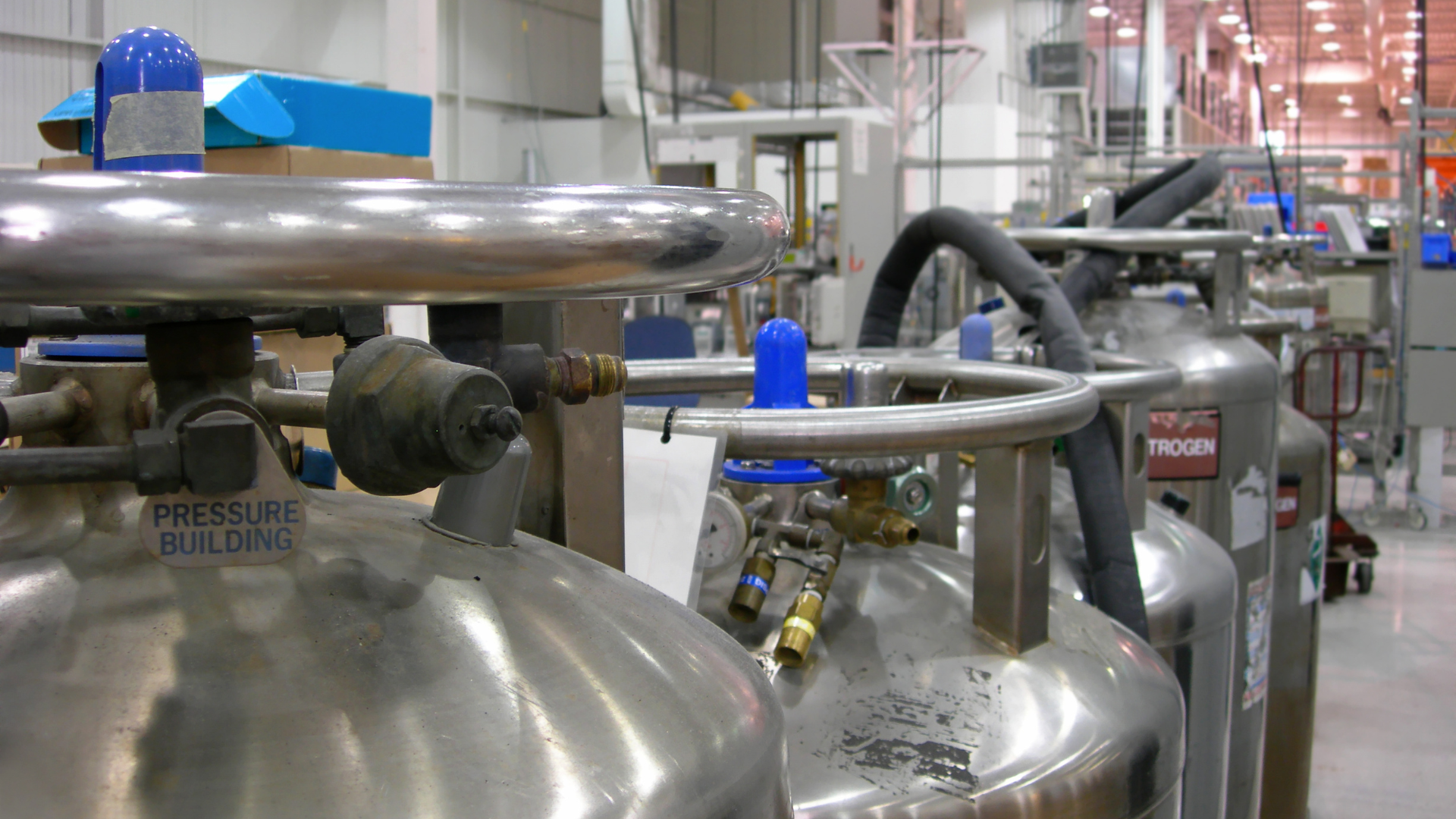 A row of stainless steel tanks are lined up in a room.