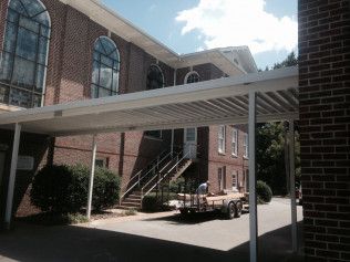 A truck is parked under a canopy in front of a brick building.