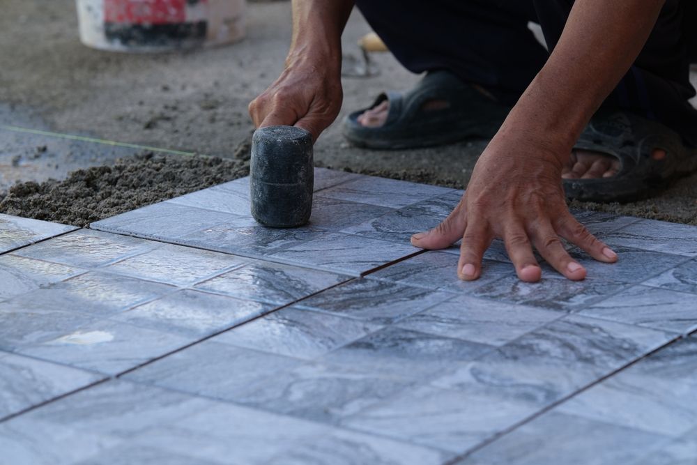 A man is laying tiles on the ground with a hammer.