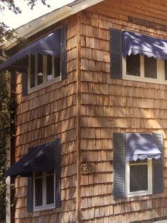 A wooden house with a blue awning on the windows.