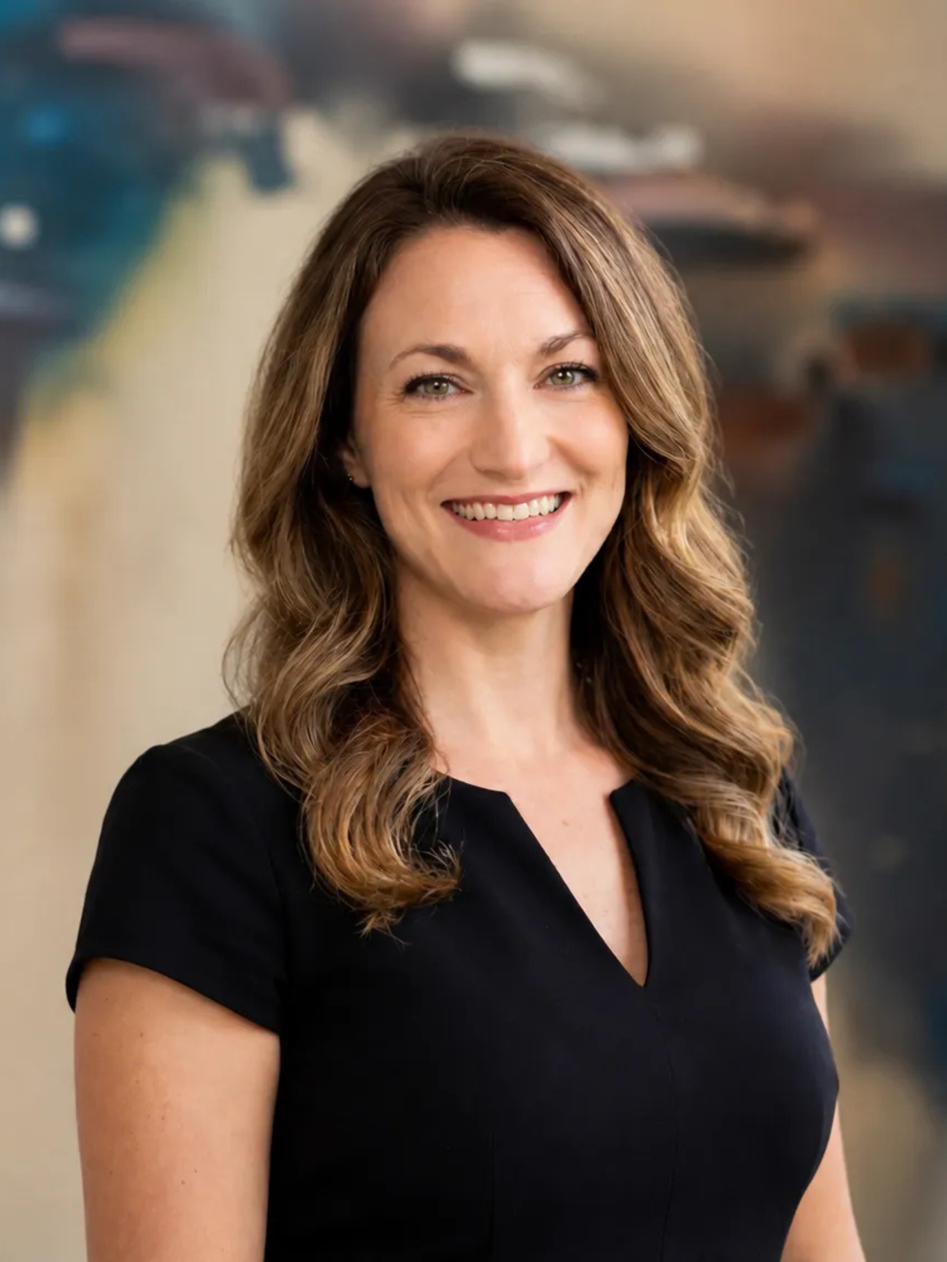 Jade Purdy wearing glasses and a white shirt is smiling in front of a painting.