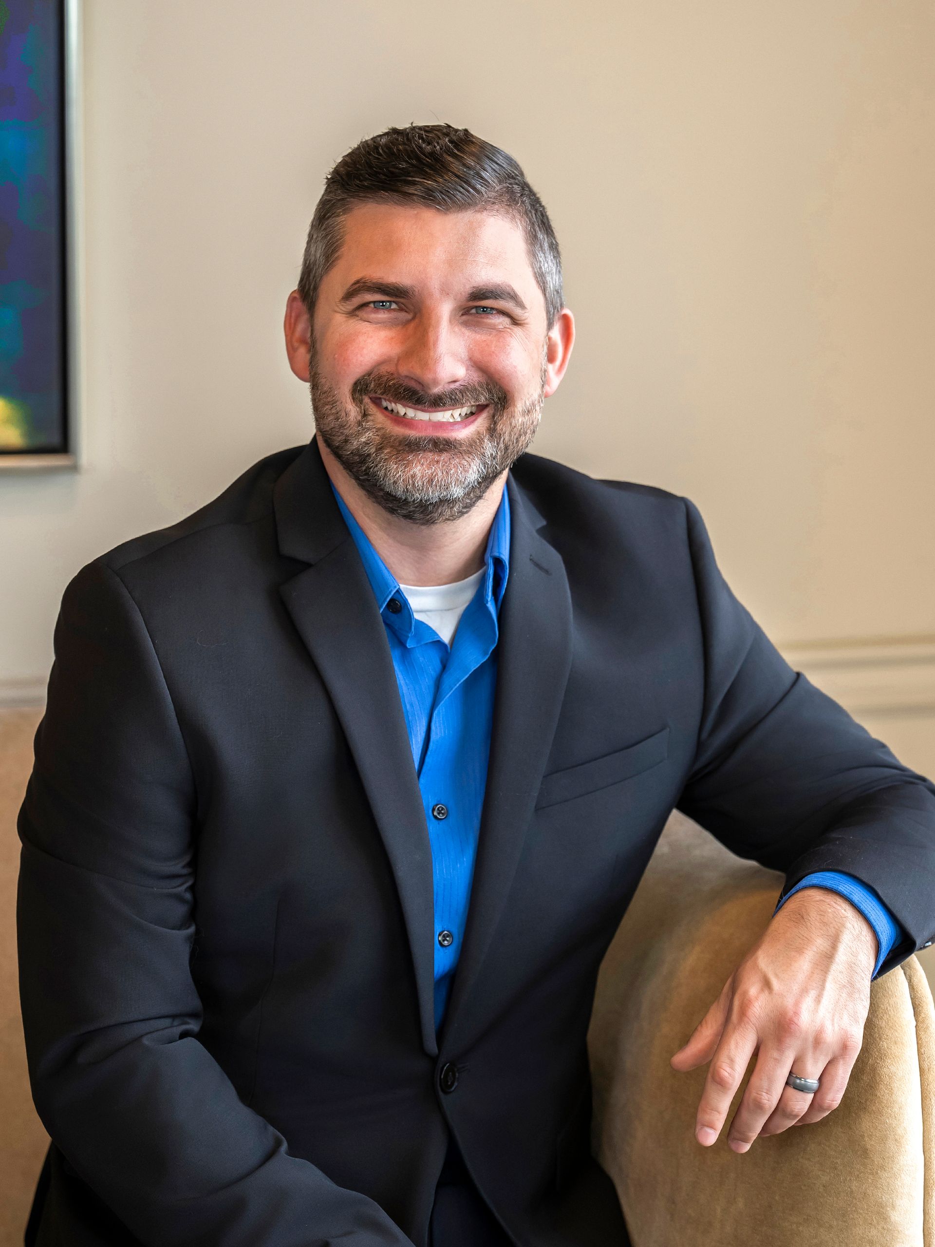 Caleb Patton in a suit and blue shirt is standing in front of a painting.