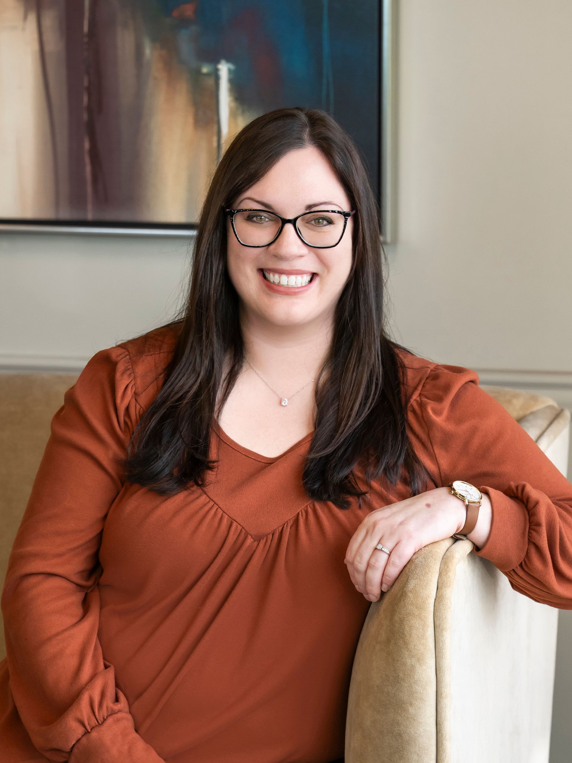 Jade Purdy wearing glasses and a white shirt is smiling in front of a painting.