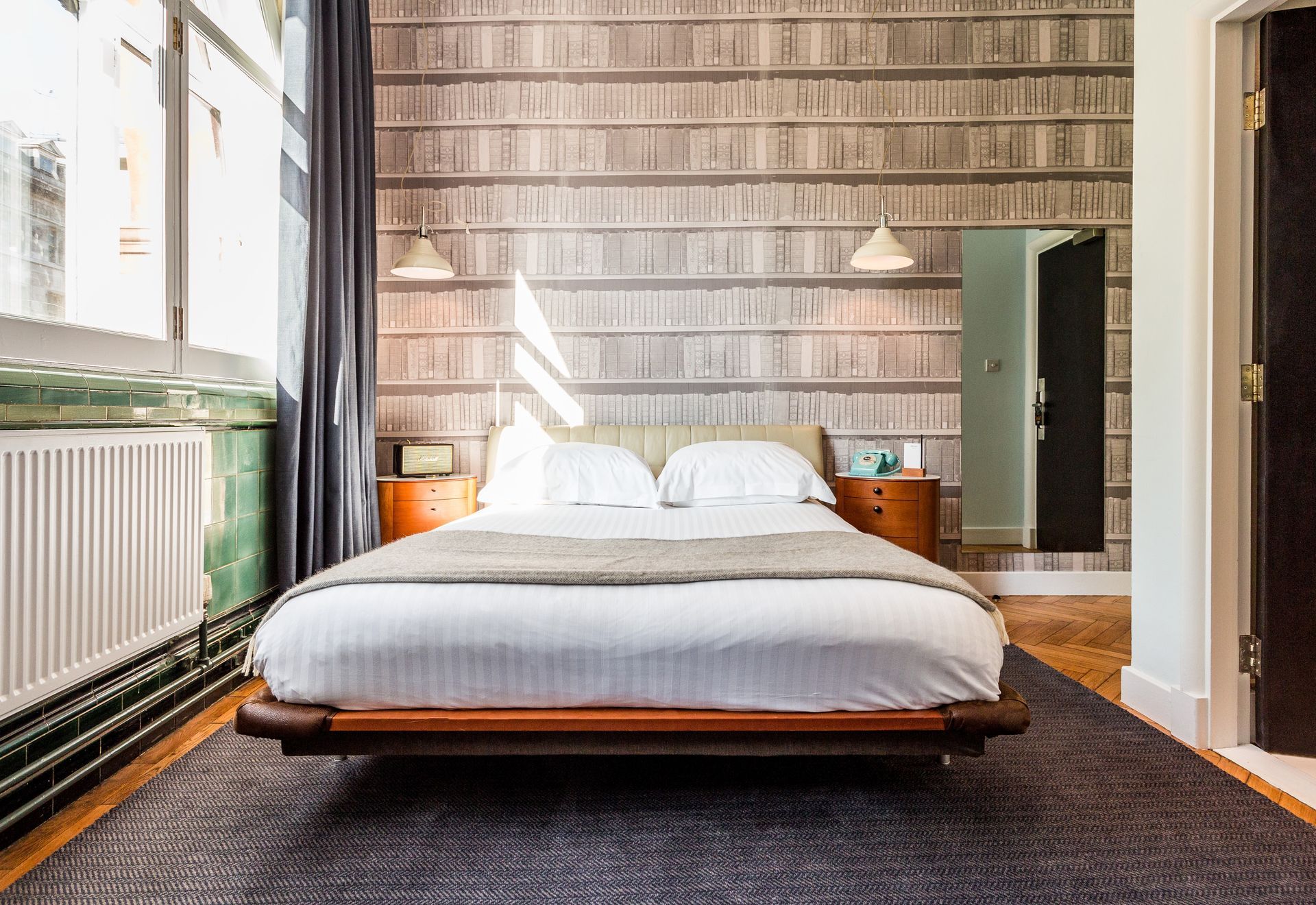 Bedroom with a floating bed, nightstands, wallpaper resembling bookshelves, and a large window.