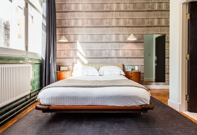 Bedroom with a floating bed, nightstands, wallpaper resembling bookshelves, and a large window.