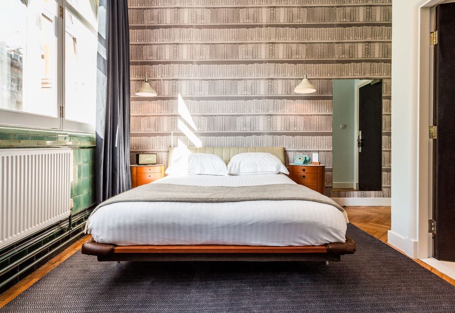 Bedroom with a floating bed, nightstands, wallpaper resembling bookshelves, and a large window.