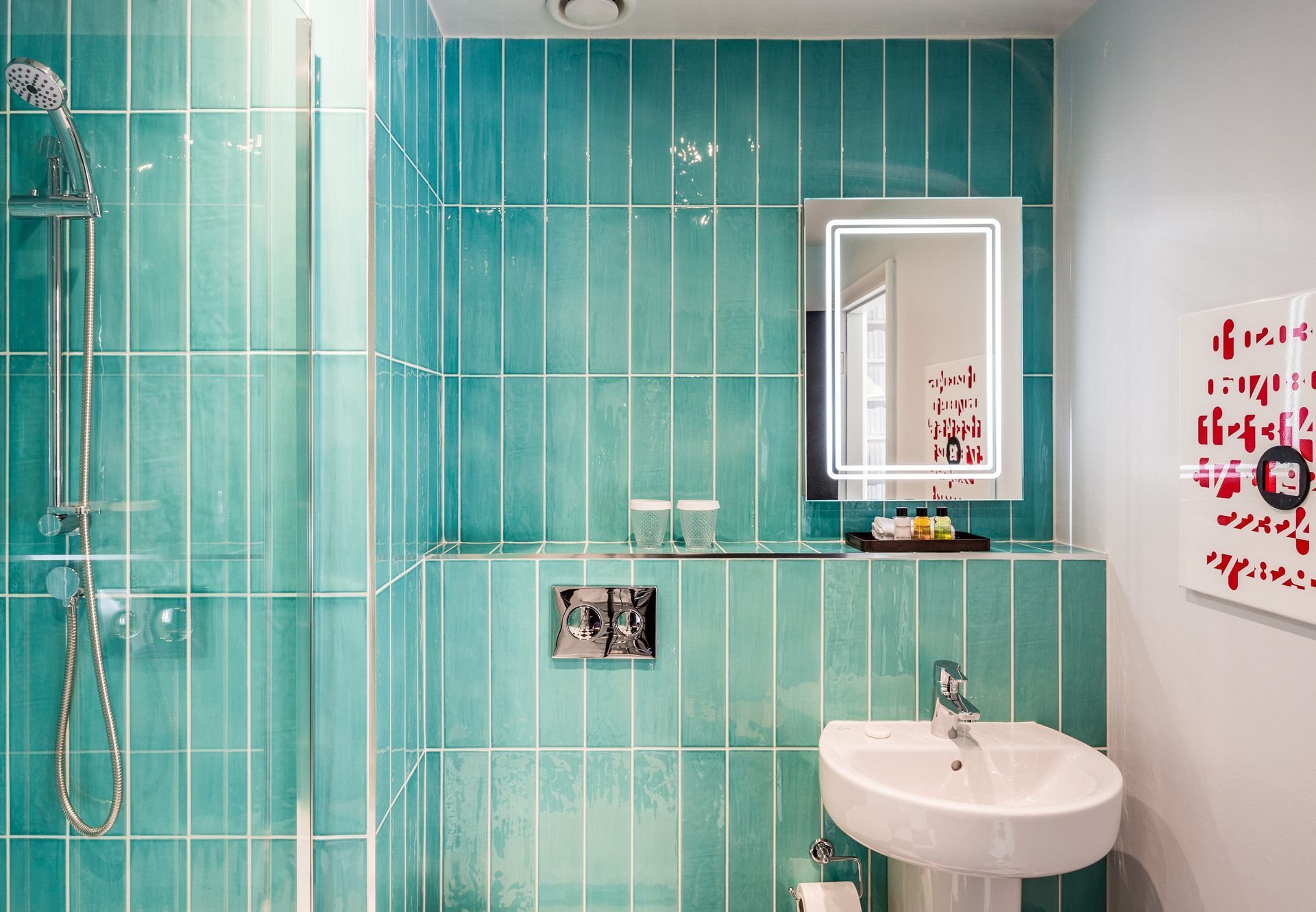 Teal-tiled bathroom with shower, white sink, and illuminated mirror. Modern design.