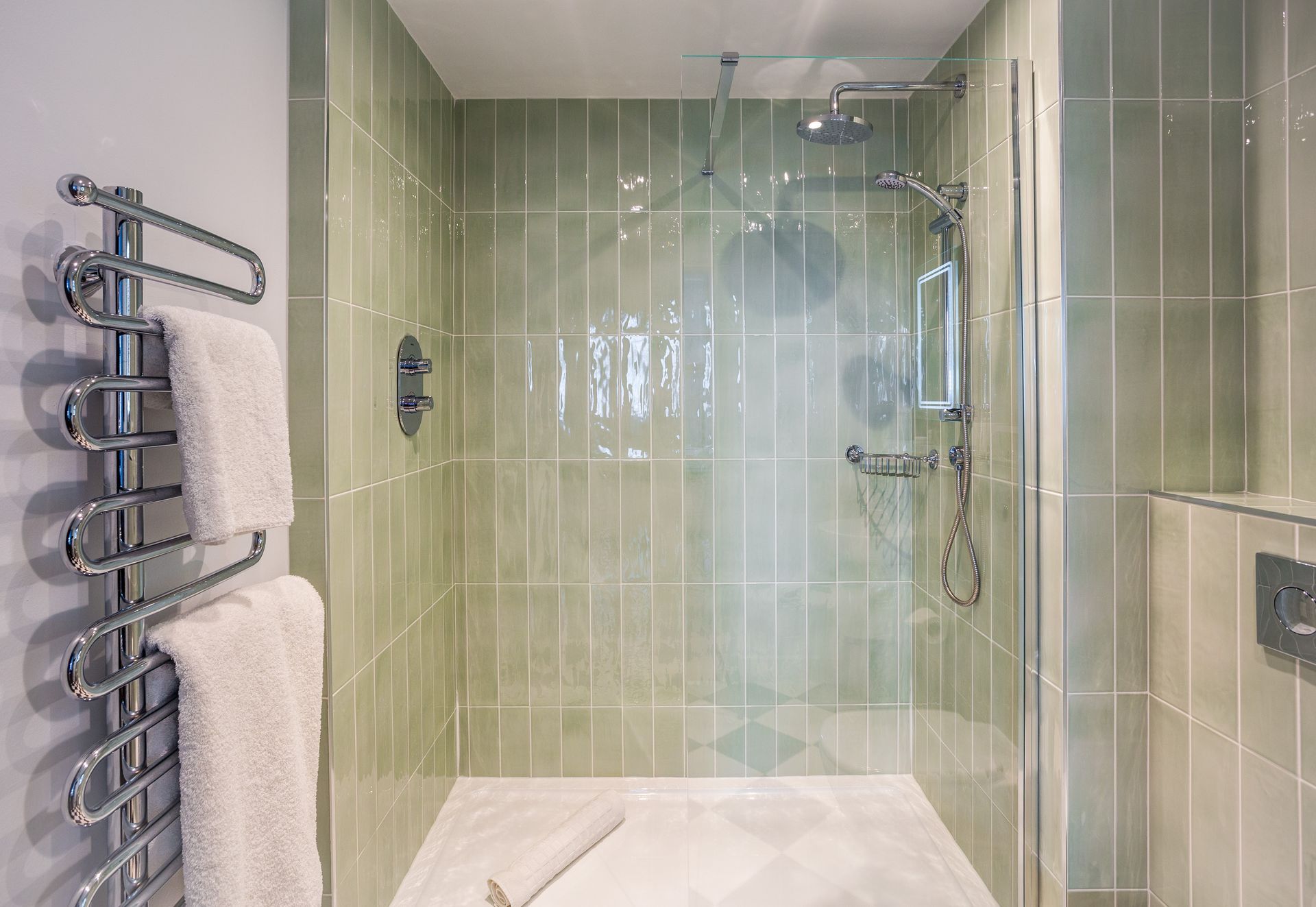 A modern bathroom with a walk-in shower, green tiled walls, and a towel rack.