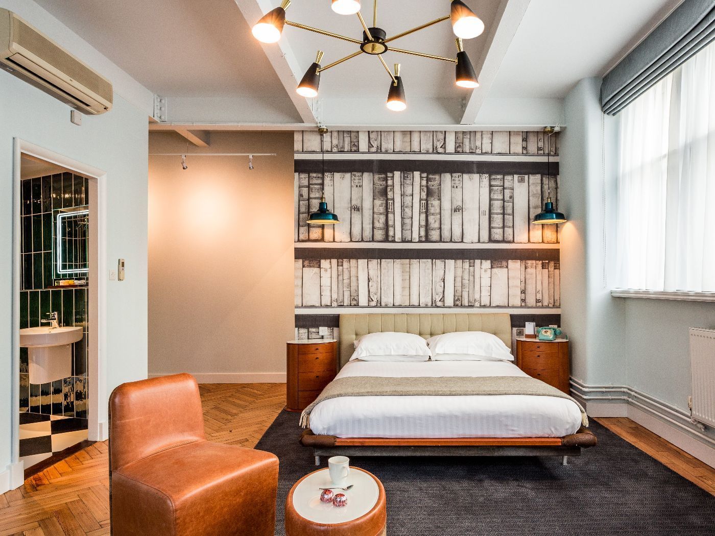 Bedroom with bed, wooden wall, brown chair, small table, and chandelier.