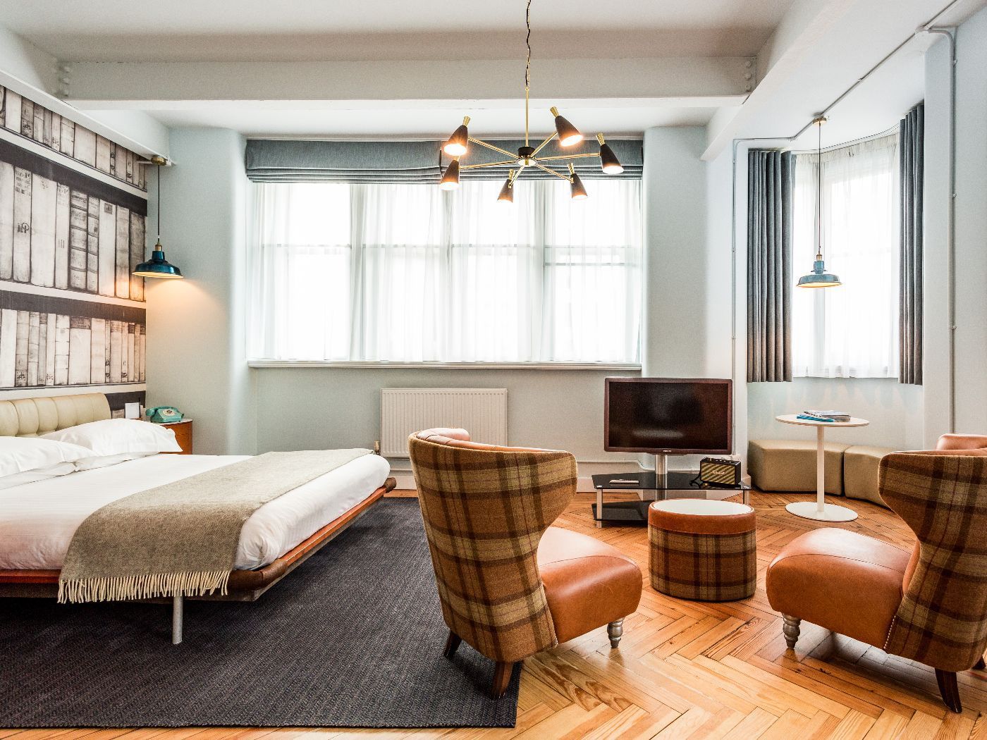 Bedroom with a bed, two armchairs, TV, and a large window with a bookshelf wallpaper backdrop.