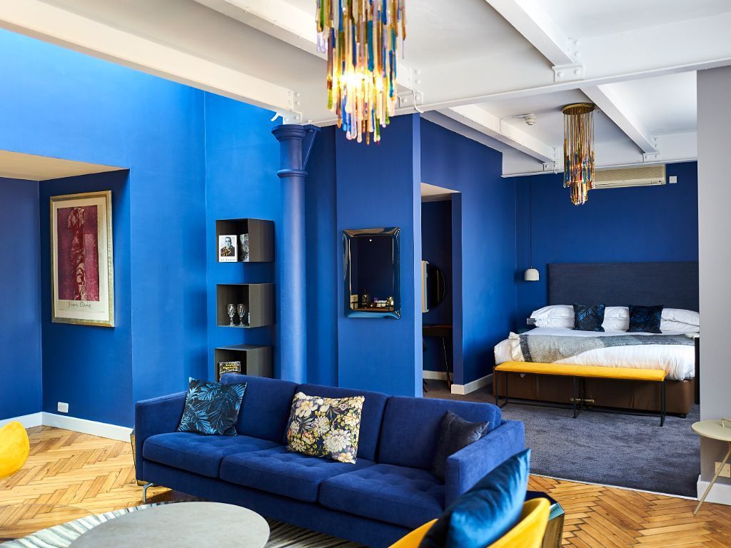 Blue-walled luxury living room with sofa, bed, and colorful chandelier.