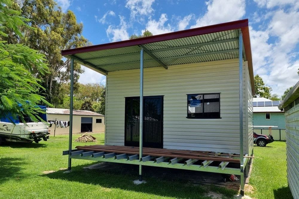 A Small White House with A Red Roof Is Sitting on Top of A Lush Green Field — All Steel Homes in Bundaberg, QLD