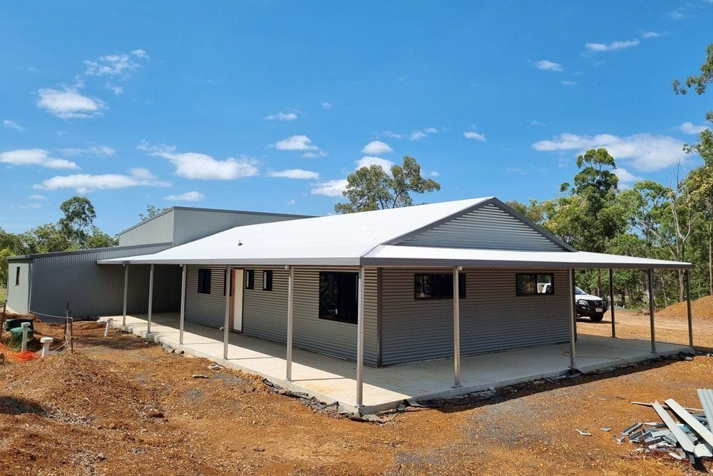 A House with A White Roof Is Being Built in The Middle of A Dirt Field — All Steel Homes in Childers, QLD