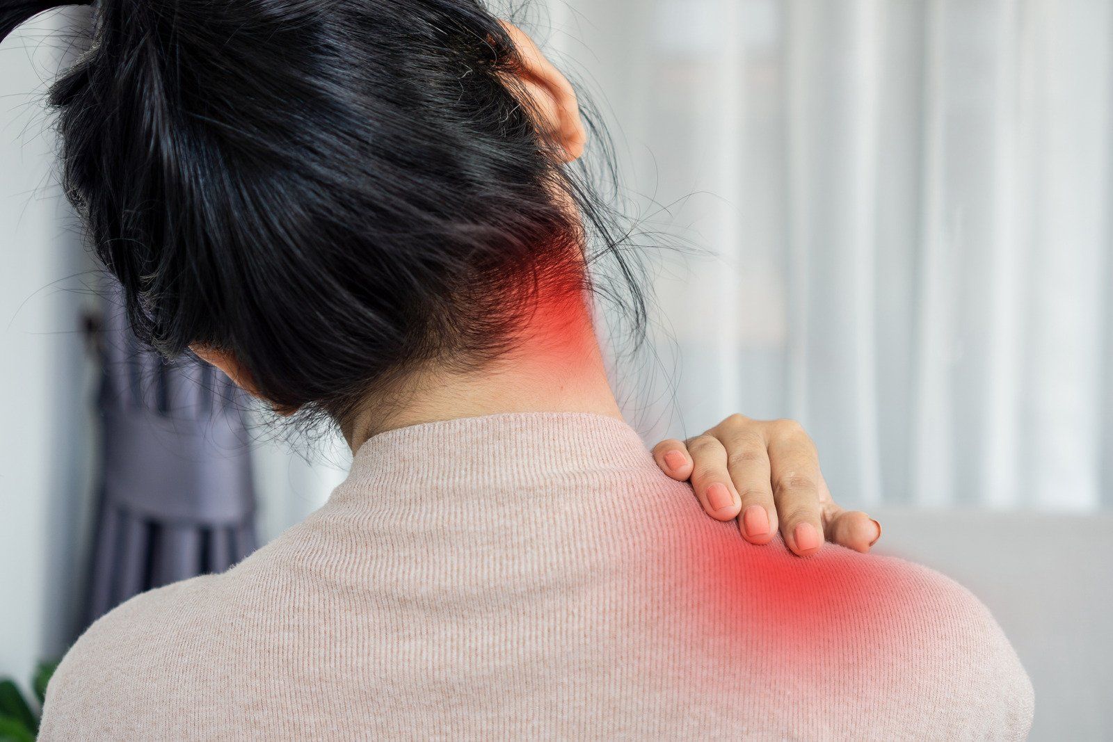 A woman is holding her neck and shoulder in pain.