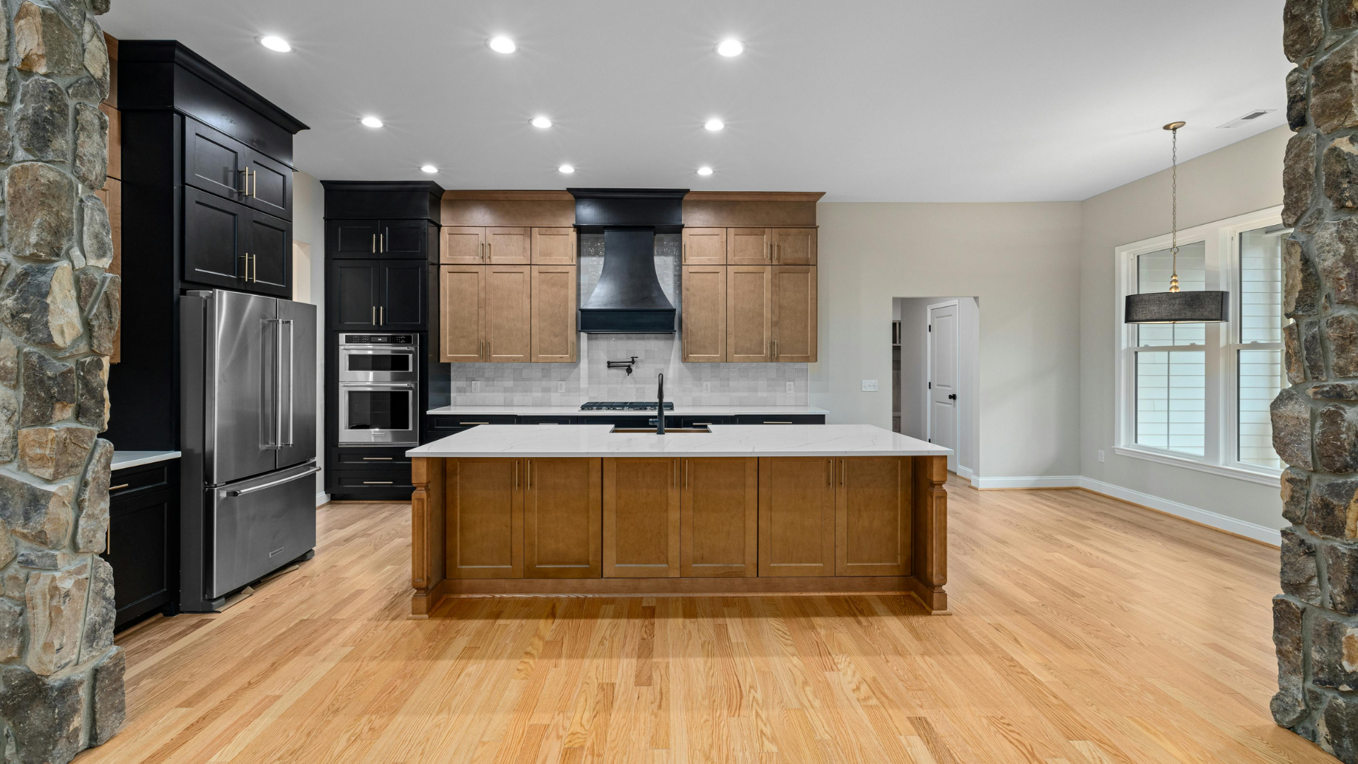 Spacious kitchen with light wood floors, cabinetry, and white countertops. Black range hood, stainless steel appliances.