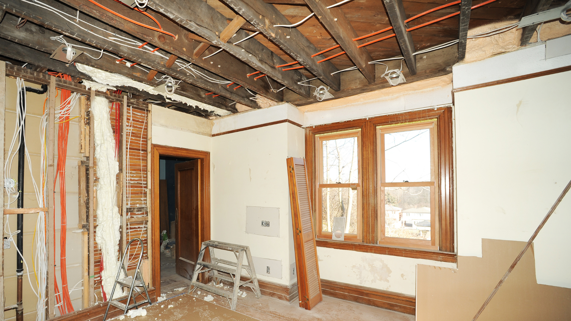 Interior room under renovation, exposed ceiling, walls, doorway, and window, with a ladder present.