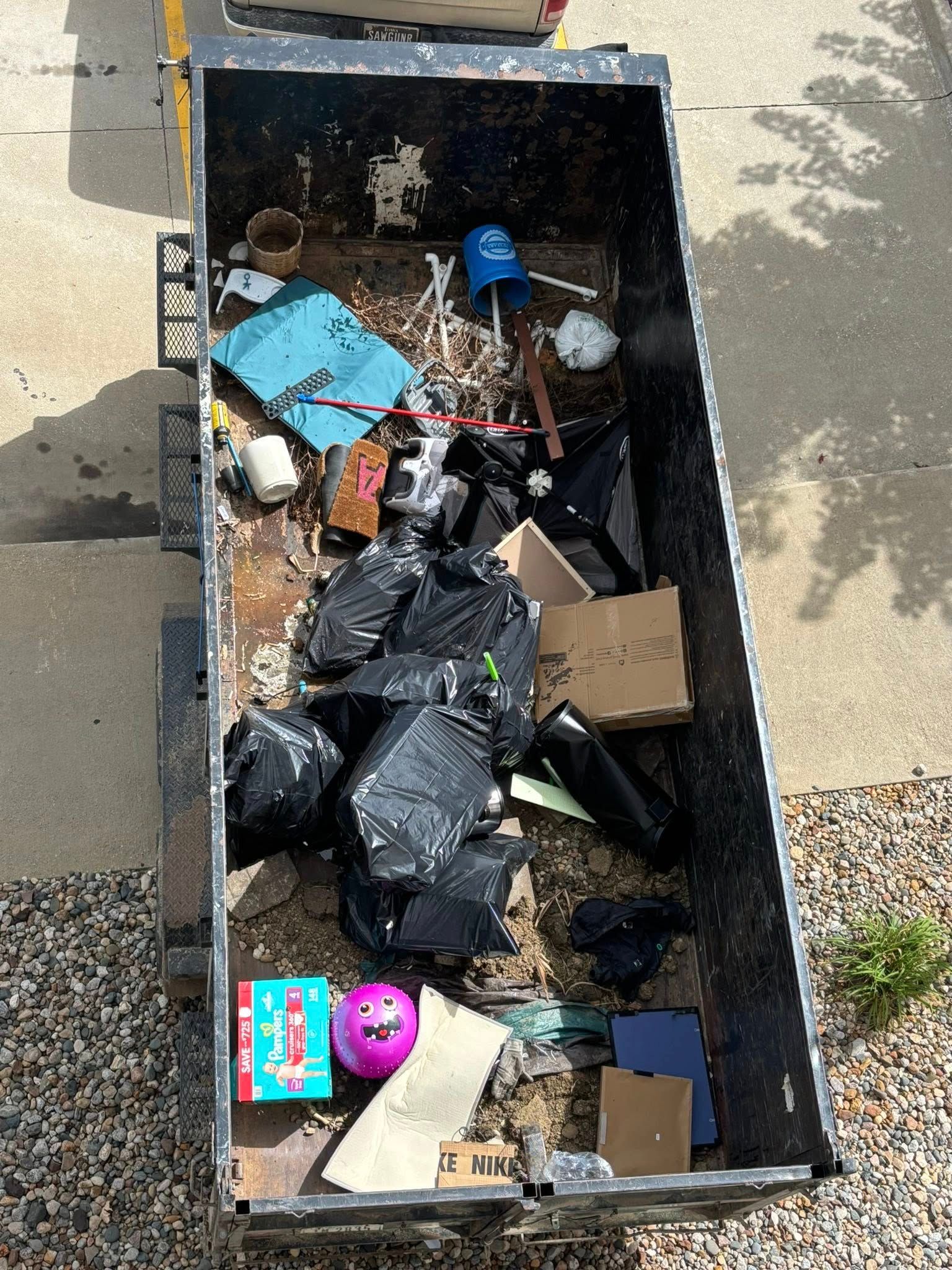 Overhead view of a dumpster filled with trash bags, cardboard, and other debris.