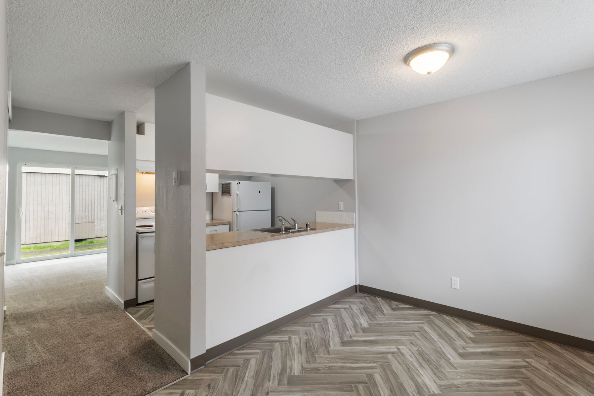 A living room with a kitchen in the background and a sliding glass door.