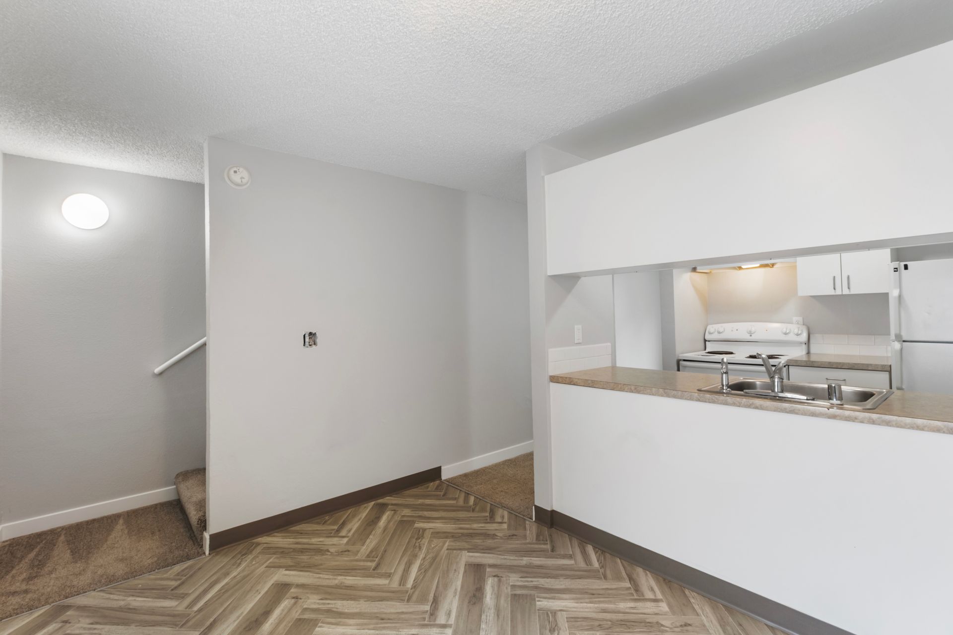 An empty apartment with a kitchen , dining room , and stairs.