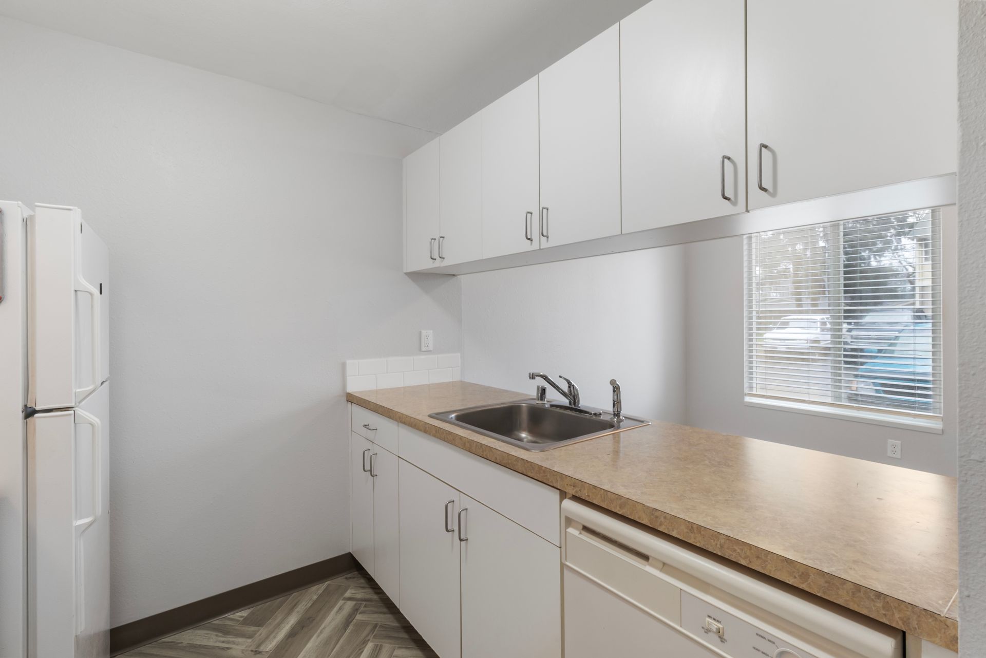 A kitchen with white cabinets , a sink , a refrigerator and a dishwasher.